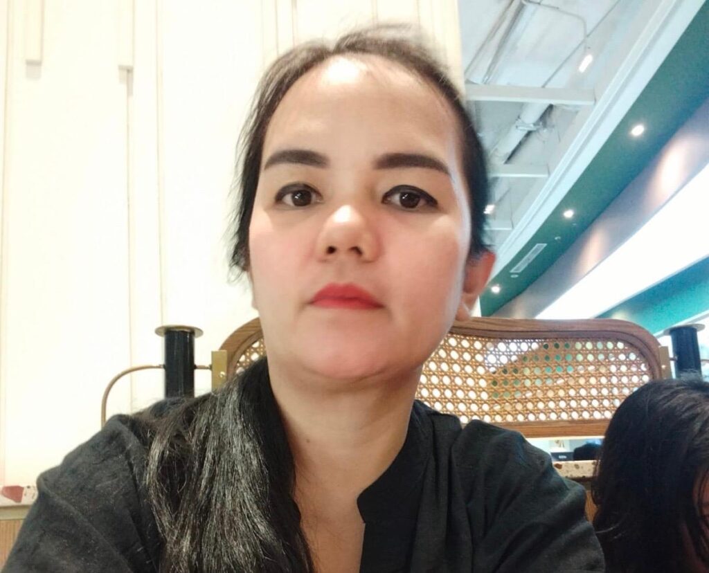 Sisca lumbantoruan catrawarta Close up portrait of a woman with dark hair wearing a black top looking at the camera indoors with a woven chair behind her